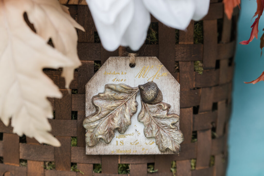 Close-up photo of tag hanging on front door fall floral basket. Tag made with resin using the IOD acorn and leaves mold.
