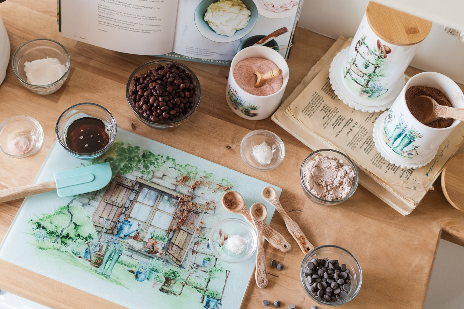 Kitchen prep area on a butcher block with a glass cutting board as a prep surface and watercolour country garden-themed canisters.