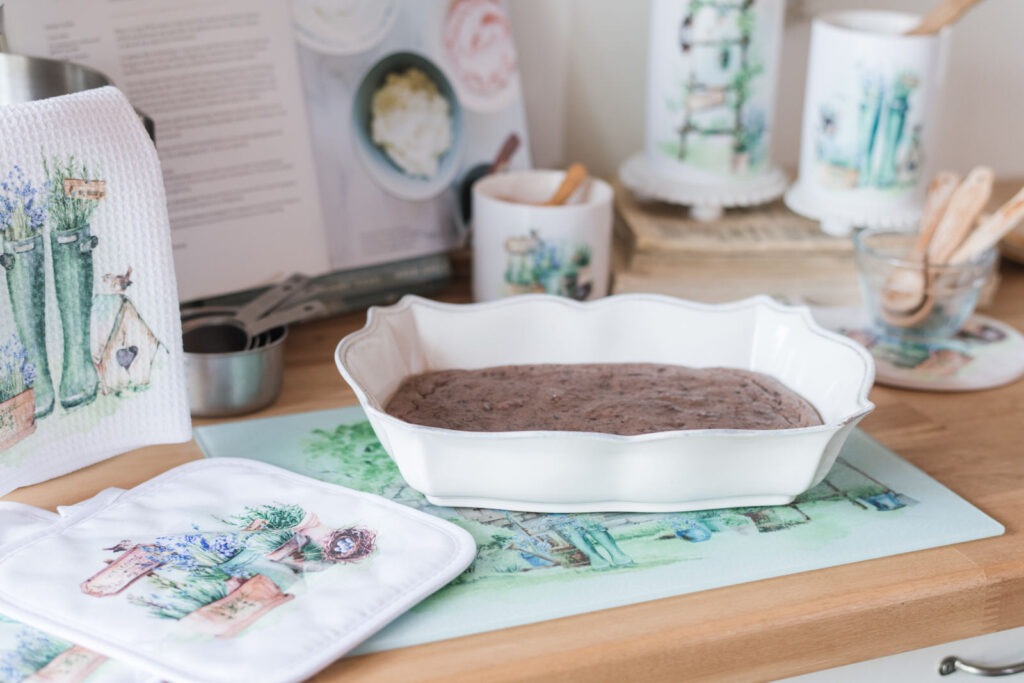 Hot baking dish, sitting on a protective glass, cutting board with potholders and other kitchen essentials 