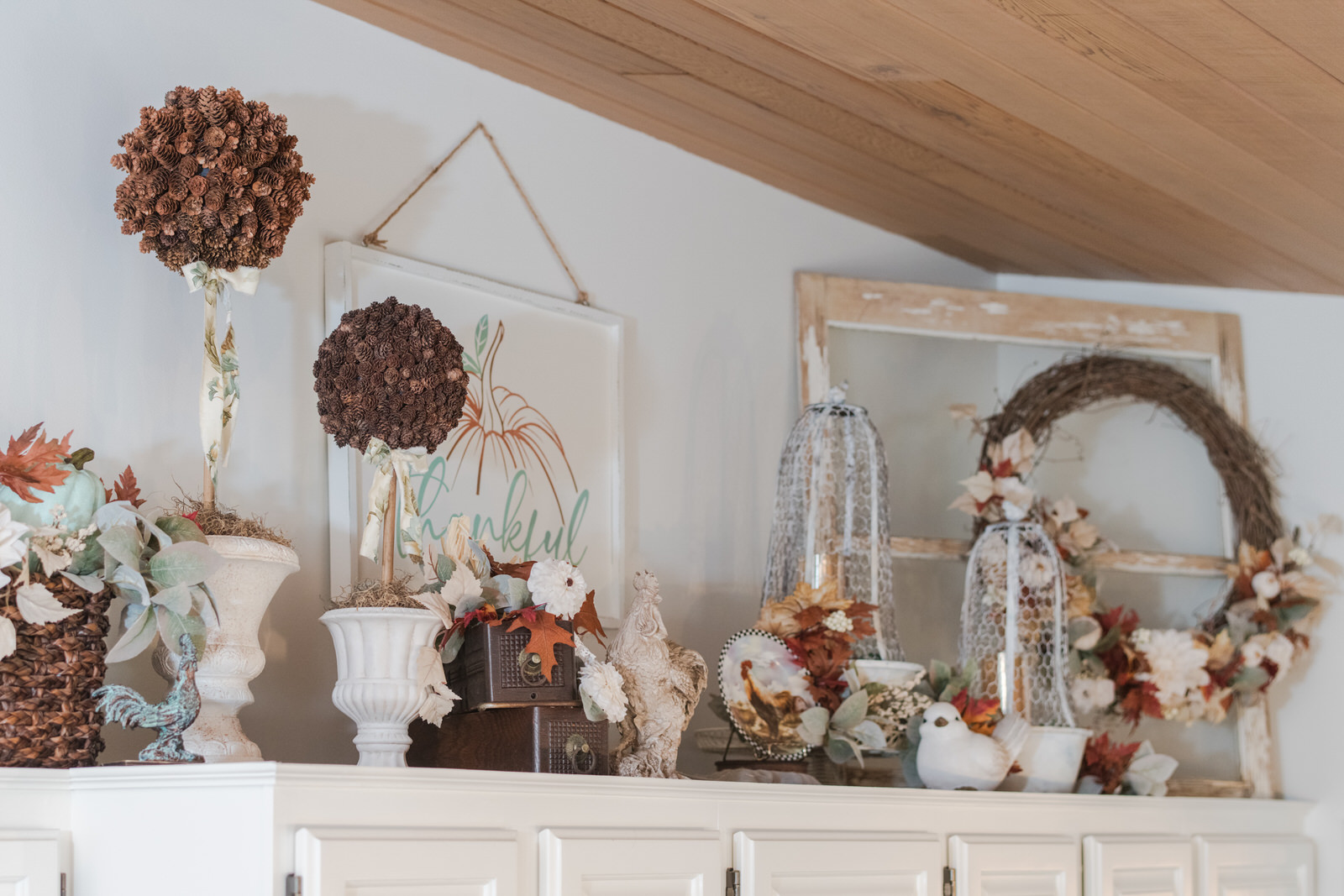 Fall kitchen decor above the kitchen cupboards. Styled with fall florals pinecone topiaries, wired cloche, roosters and more.