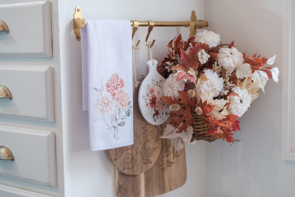 Spicy floral, fall, tea, towel, hanging with wood for cutting boards in a basket of flowers at the end of a cupboard
