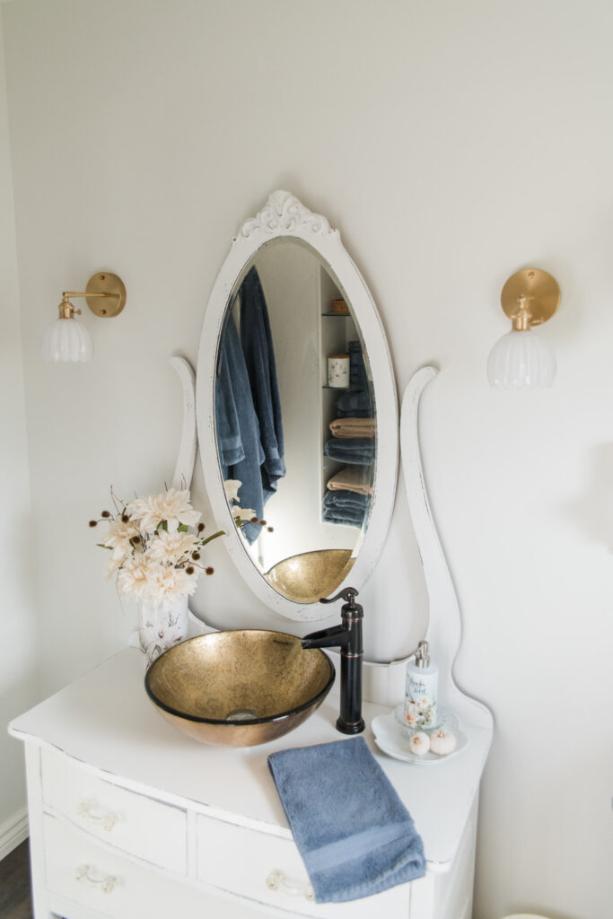Simple bathroom refresh with fresh paint, warm brass lighting, and soft autumn cottage-style decor.