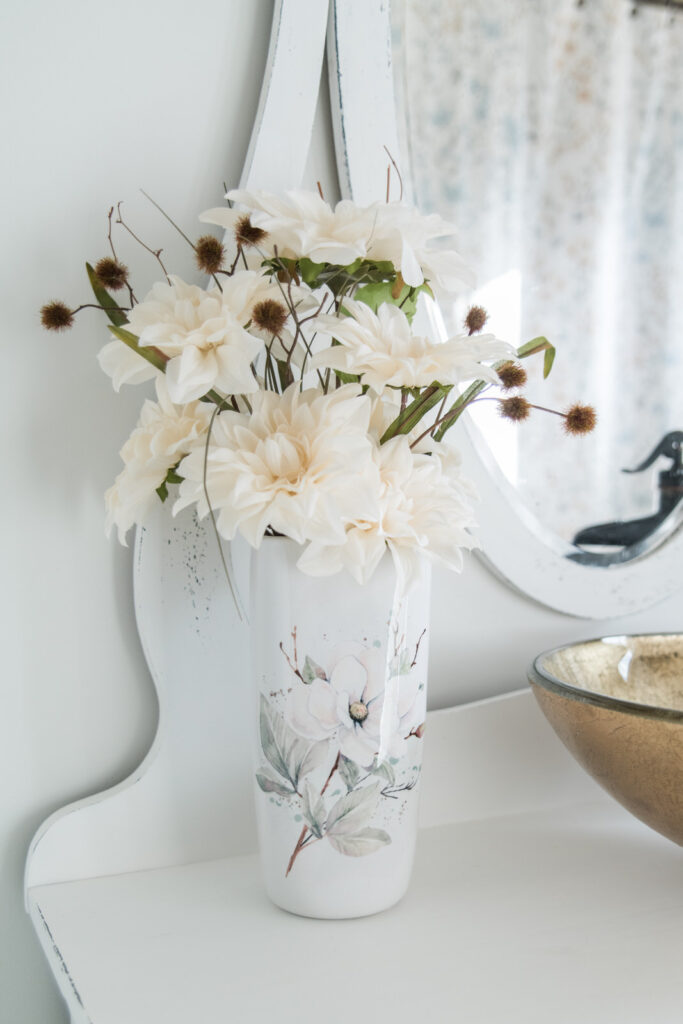 Fall florals in a white ceramic vase with magnolias. Sitting on a vintage bathroom vanity in a cottage makeover bathroom. 