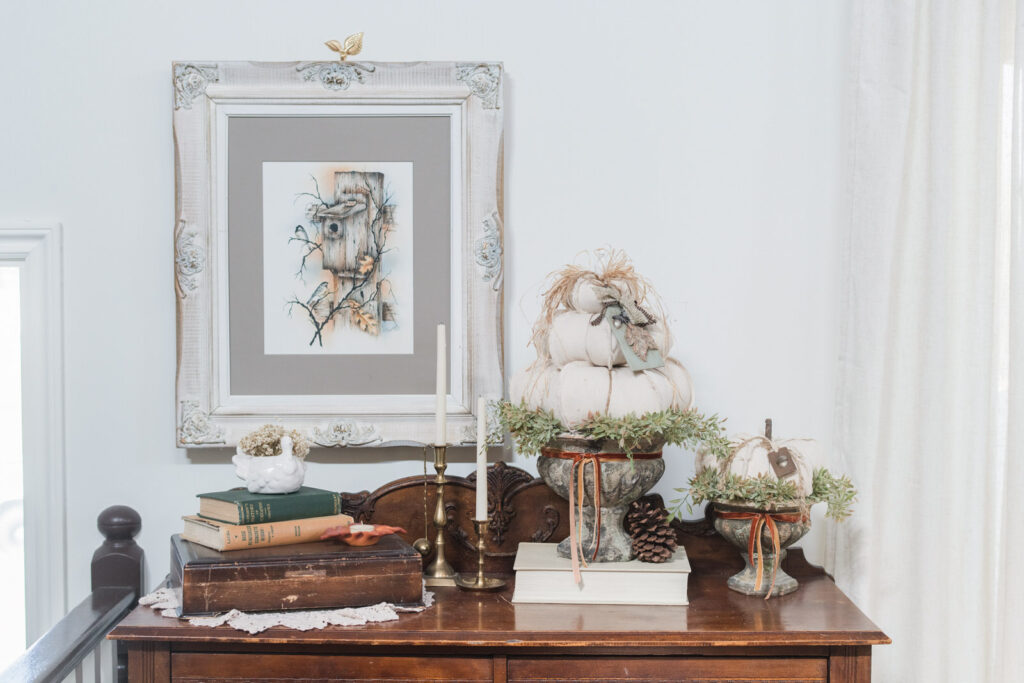Antique wooden cabinet styled for fall with framed painting and DIY pumpkin topiaries