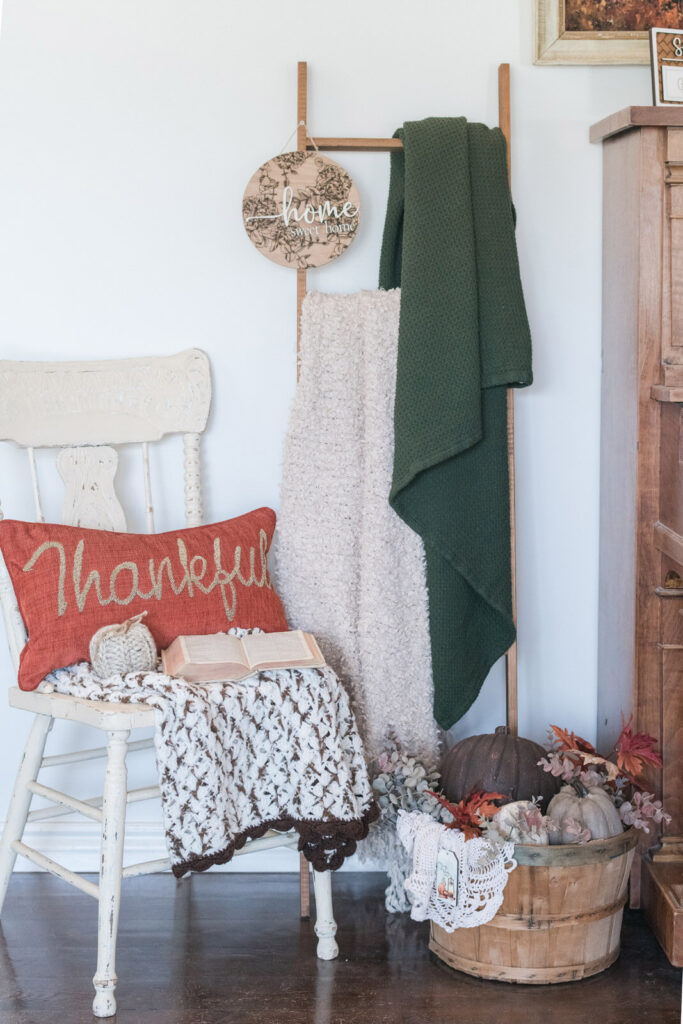 Wooden blanket ladder with cream and green throws beside an apple barrel full of pumpkins