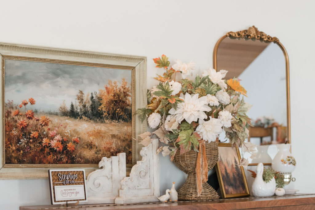 Fall piano vignette with thrifted landscape print, wicker vase of autumn florals, and Scripture sign