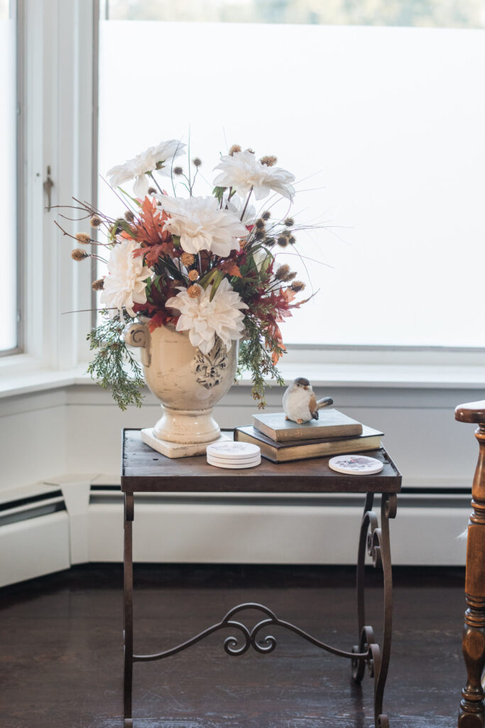 Wrought iron side table styled with cream florals, russet leaves, and vintage books