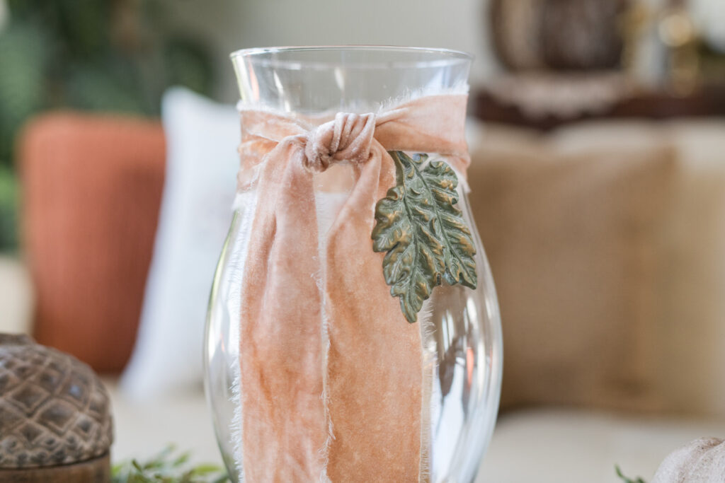 Candle with velvet ribbon on fall coffee table beside rustic basket of gourds