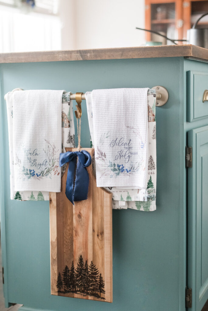 Hope Has Come tea towels layered over other towels hanging on the end of the kitchen island with a forest cutting borad 