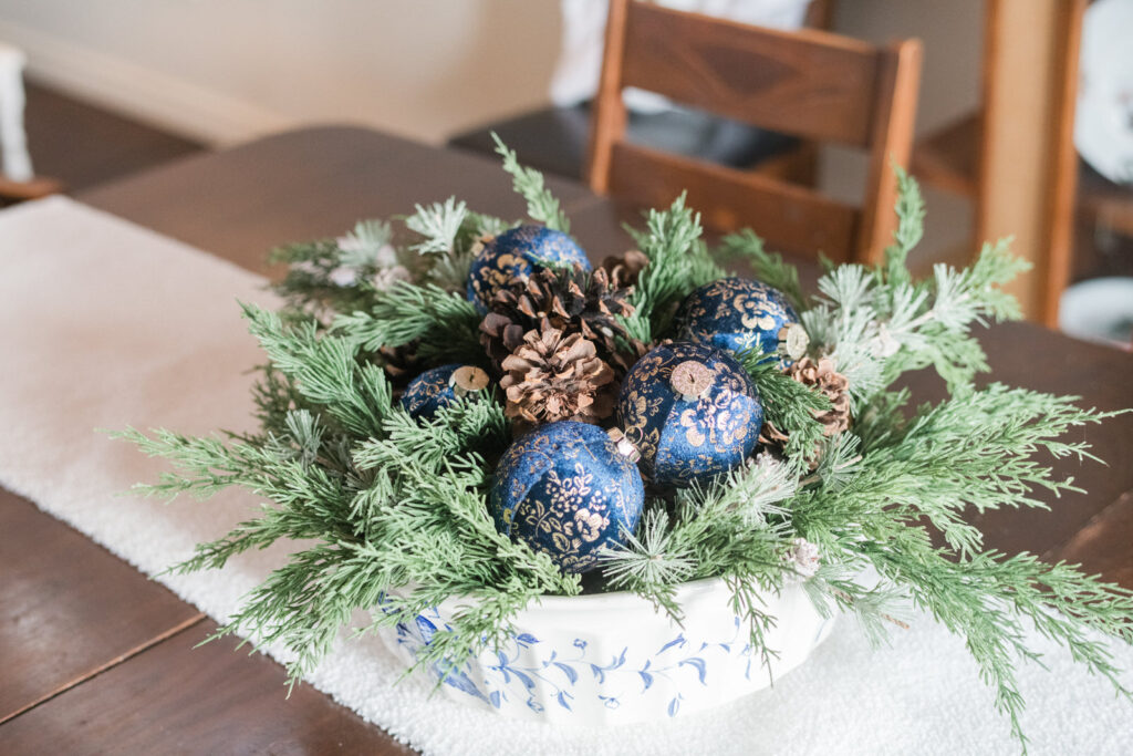 Blue and white farmhouse bowl centerpiece with pinecones, greenery, and navy ornaments
