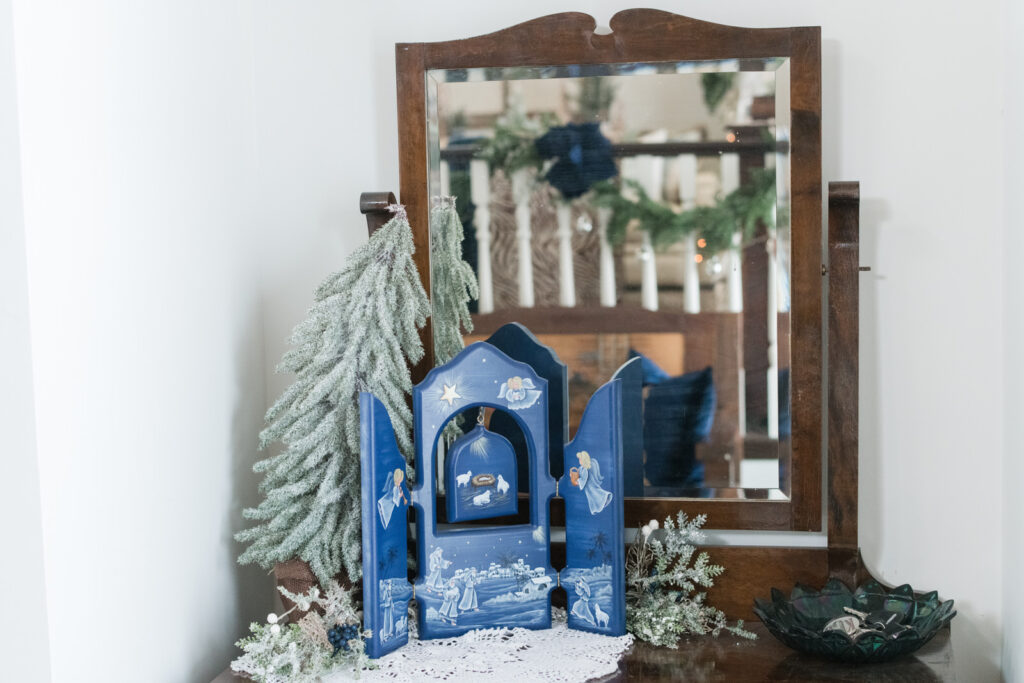 Christmas entryway with navy and gold decor and antique dresser with nativity display.