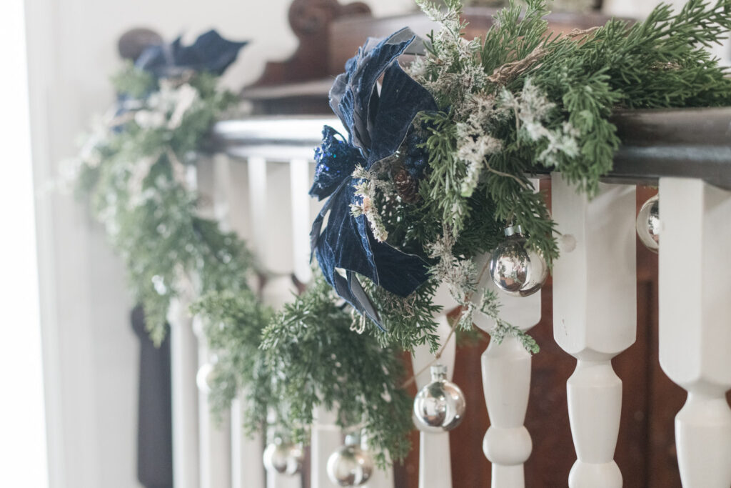 Soft touch, greenery draped over bannister in a sunken entryway with blue velvet poinsettias and frosted floral pics added in