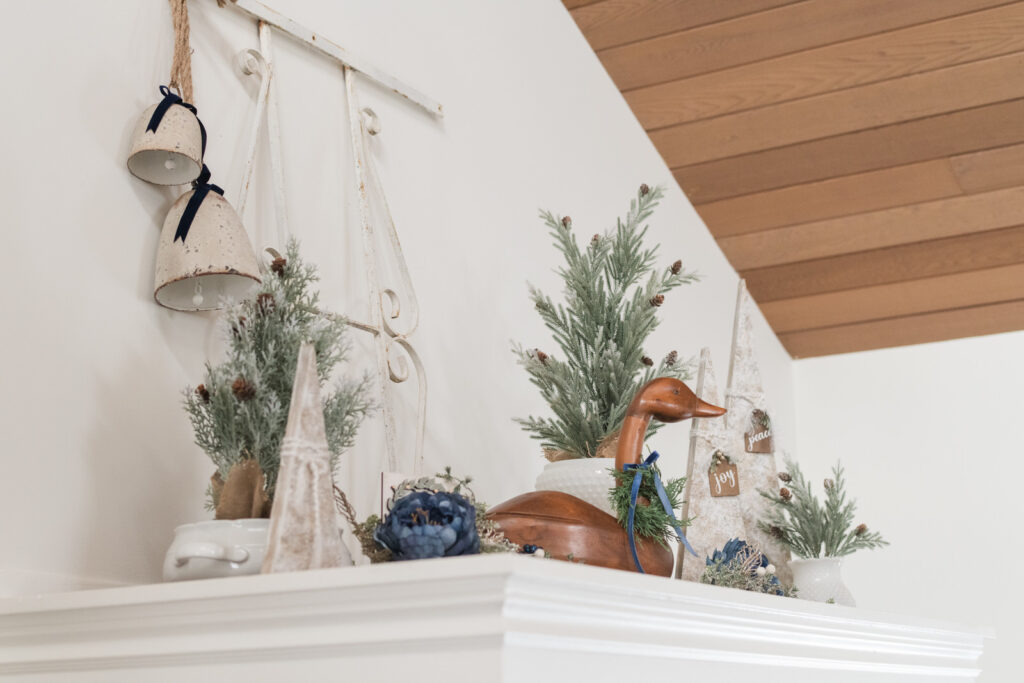 Christmas display above an entryway closet with a vintage window, grate, bells, full greenery, trees, a wooden goose and wooden trees