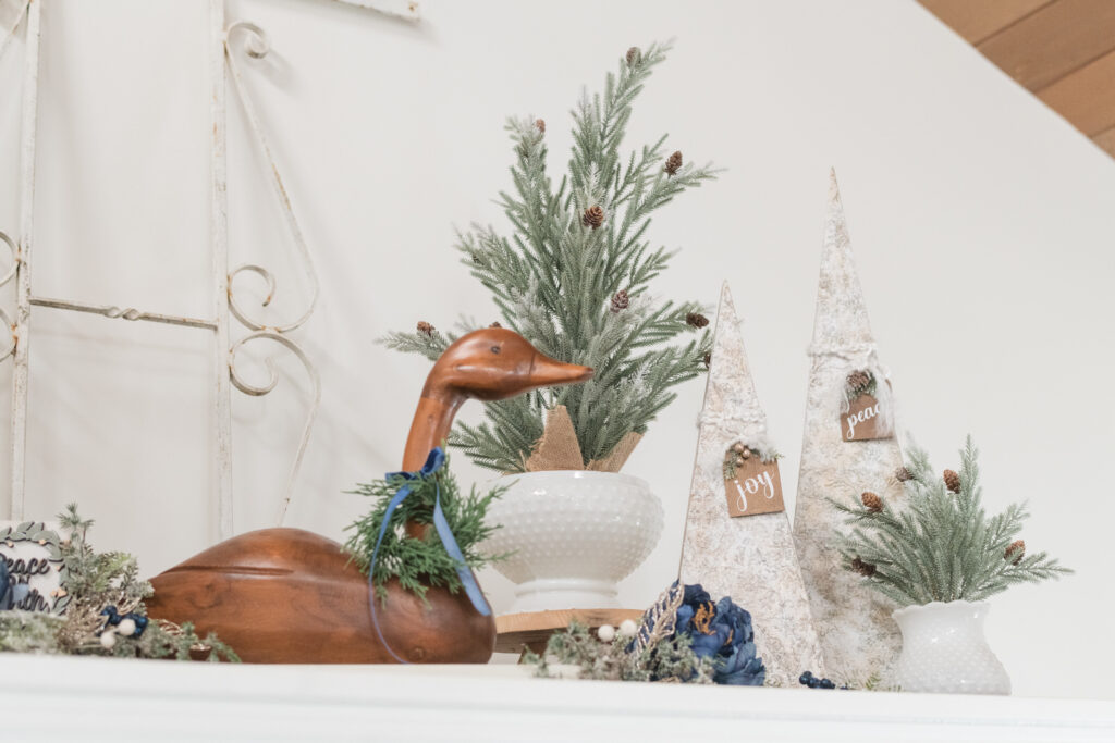 Vintage goose with a wreath and bowtie beside faux trees and DIY wooden trees.
