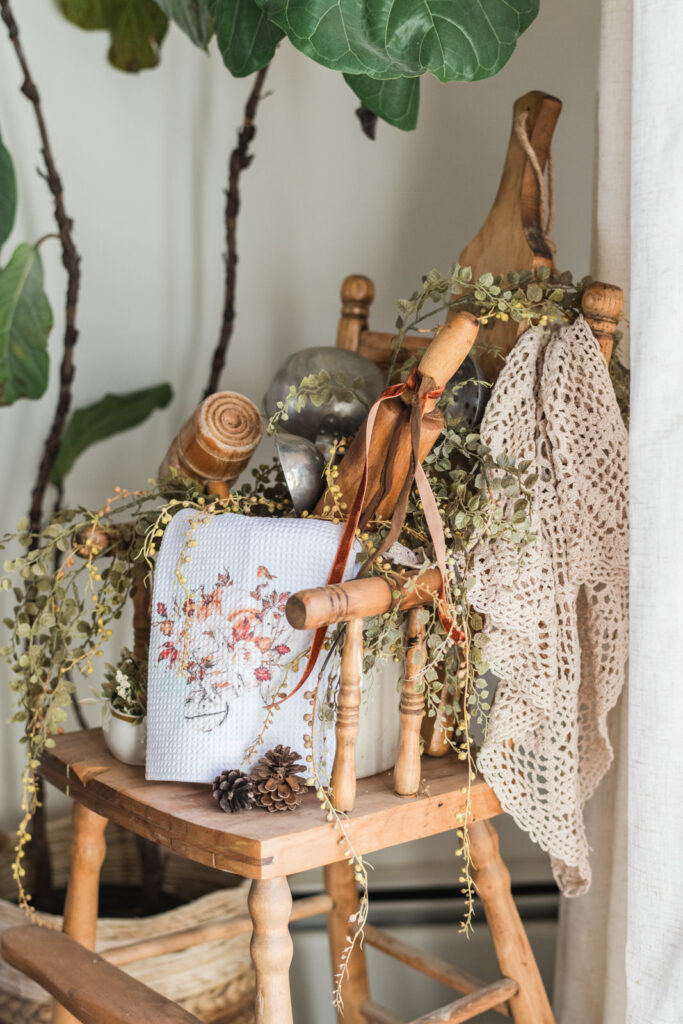 Vintage highchair styled for fall with a crock and utensils, draped with a lace tablecloth and tea, towel with some florals for fall 