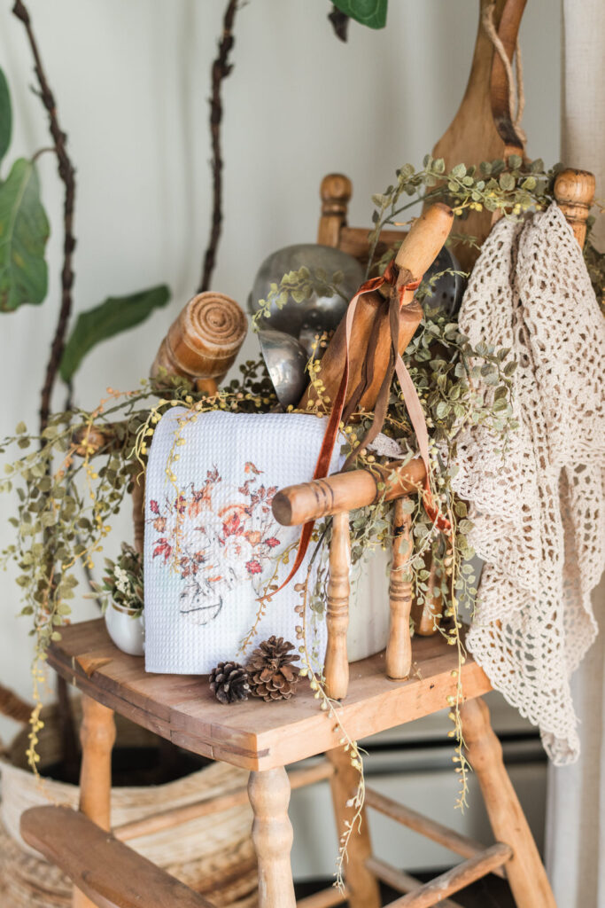 Tea towel draped over vintage crock with greenery and utensils – cozy fall kitchen styling