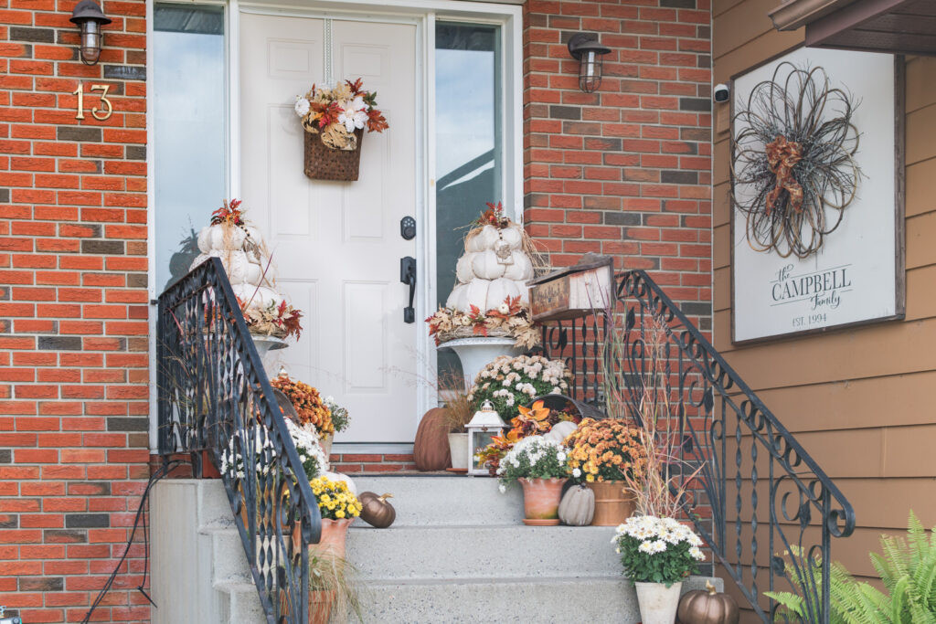 Neutral front door painted in Fusion Mineral Paint Cashmere, flanked by urns with stacked white pumpkin topiaries, mums, and fall foliage.