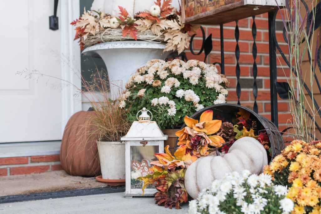 Mixture of fresh mums, dried grasses, and pumpkins in warm copper and cream tones arranged on concrete steps.