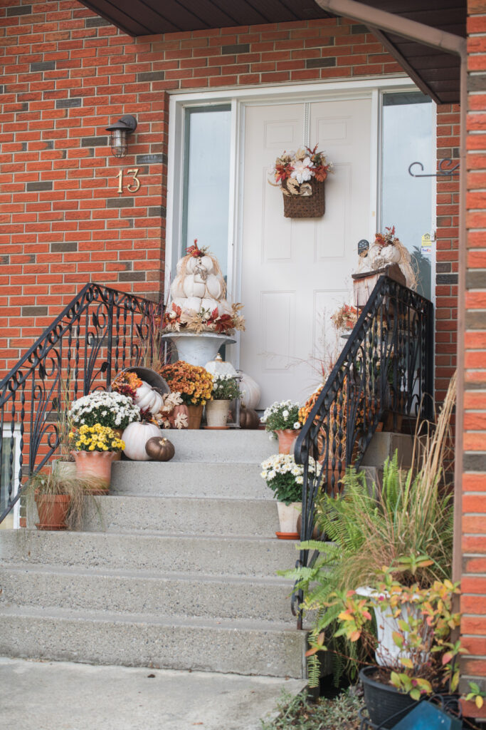 fall front step decorated with grass, mums and pumpkins