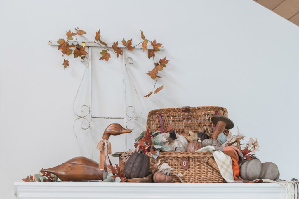 Old wicker picnic basket filled with textured pumpkins, wooden spools, and autumn florals sitting above the entry closet. With a wooden goose and wrought iron panel.