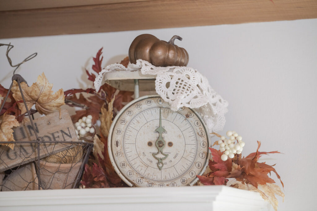 Vintage scale draped with a lace doily with a pumpkin on top, surrounded by fall foliage 