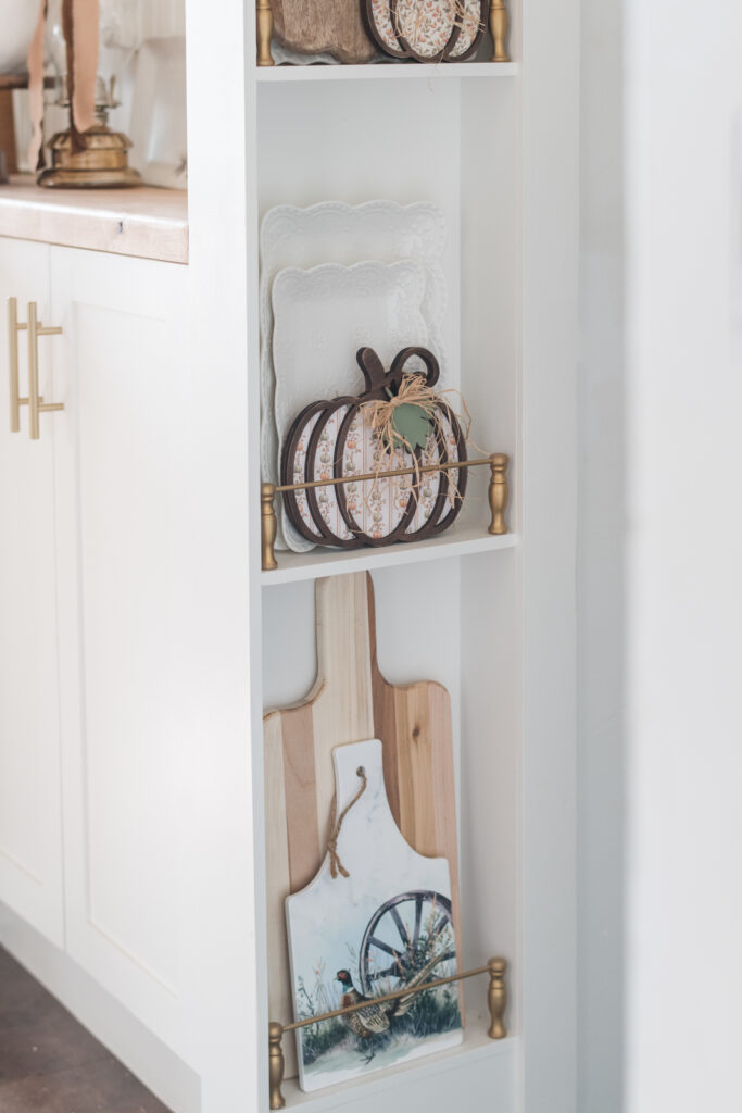 Plate rail at the end of my baking area, holding ceramic pheasant, trivet, and a wood, pumpkin and cutting boards 