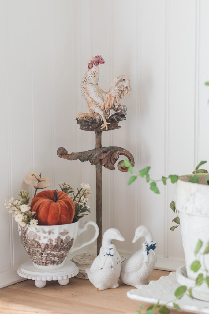 Hand crafted rooster weathervane with Thrifted, Guy, sultan, pepper shakers, and Ironstone mug with florals and a pumpkin beside herb pots 