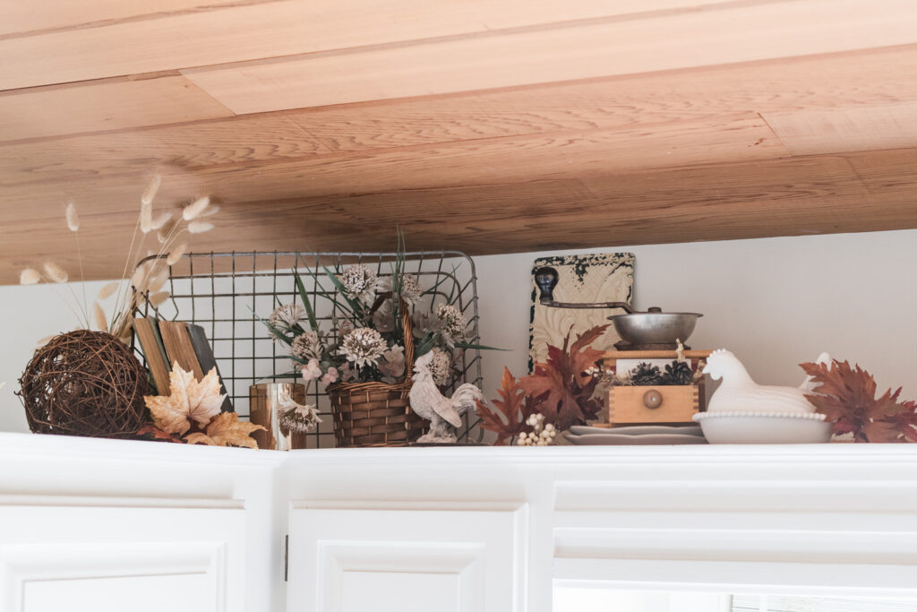 Wired crate with vintage books, fall Decour, roosters tin, tile and chicken dish with a vintage coffee grinder on top of the kitchen, covered for fall decor 