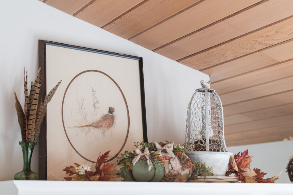 Thrifted vintage pheasant art piece beside a wired cloche with wood pumpkins and fall florals in a vase with pheasant feathers