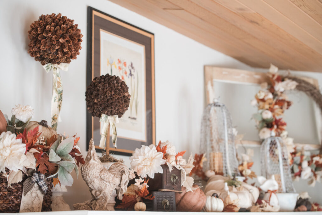 Above-cabinet styling with pinecone topiaries, wire cloches, and fall foliage.