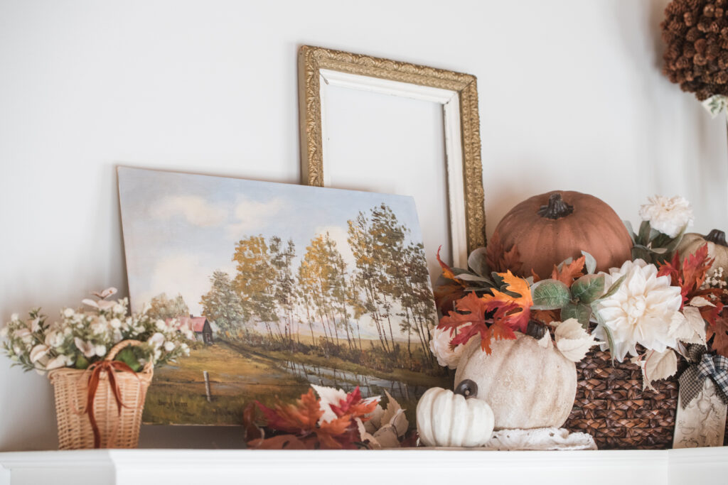 Vintage hand, painted art piece on top of the kitchen, cupboard layered with a vintage frame, and a basket full of DIY textured pumpkins with another small basket of fall florals 