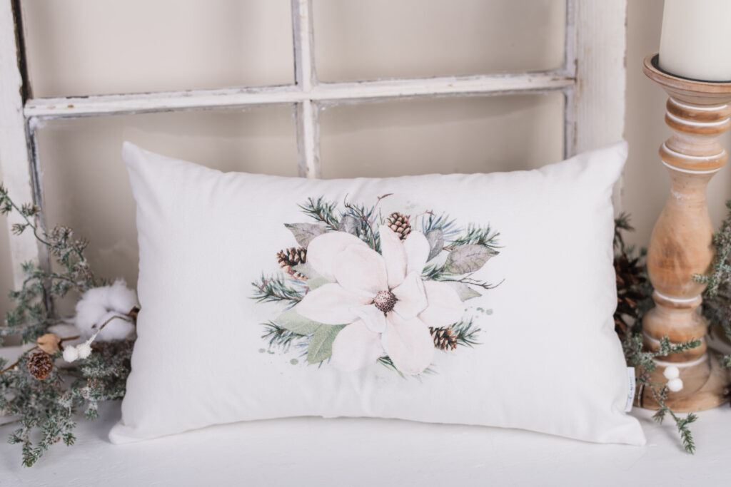 Magnolia Christmas pillows with a magnolia flower and pinecones on neutral background.