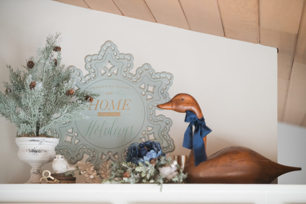 Above the cabinet, Christmas decor with a wooden goose, wearing a bow, a faux tree, and Christmas greenery and a snowflake sign 