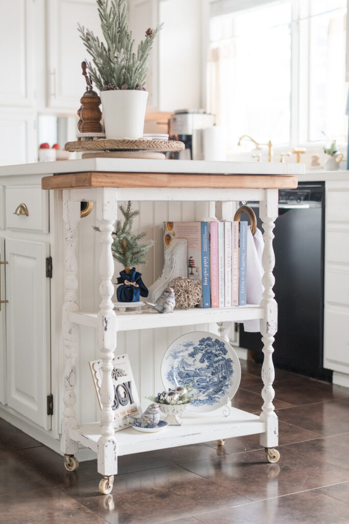 Vintage-style kitchen cart decorated for Christmas with greenery, books, and blue accents