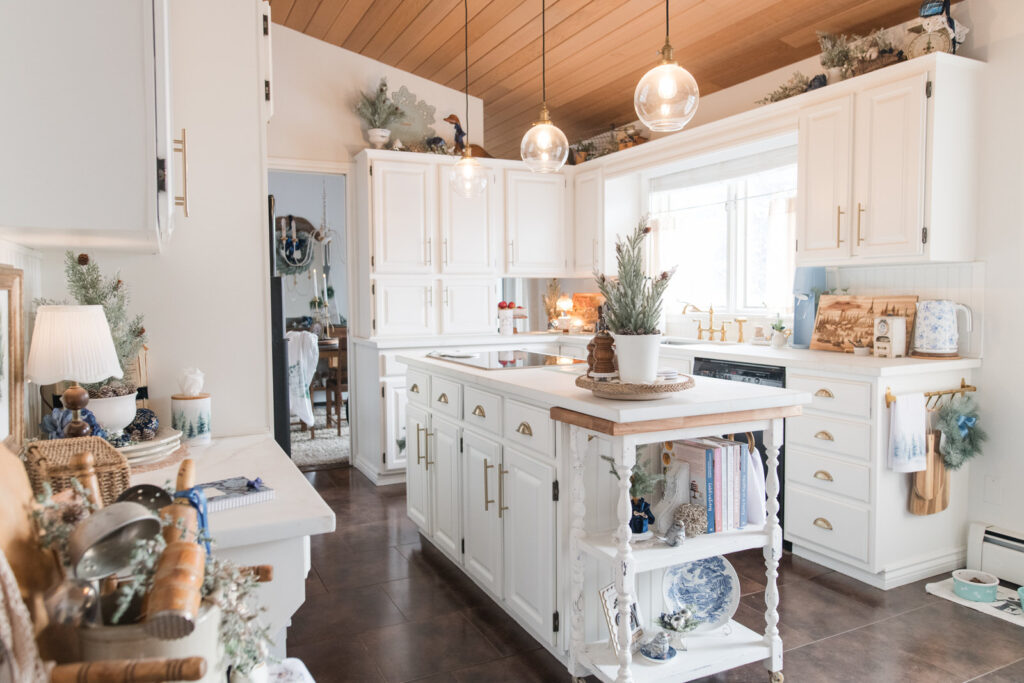 Cozy Christmas kitchen decorated in blue, white, and gold with white cabinets, wood ceiling, and vintage holiday accents