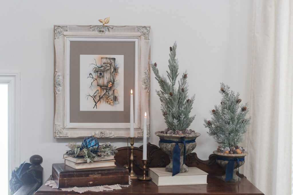 Antique cabinet styled in the living room with Christmas decor with vintage books, art, trees, and candlesticks 