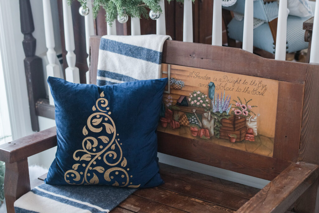 Entryway bench styled with a blue velvet and gold pillow, sitting on a blue and white striped blanket
