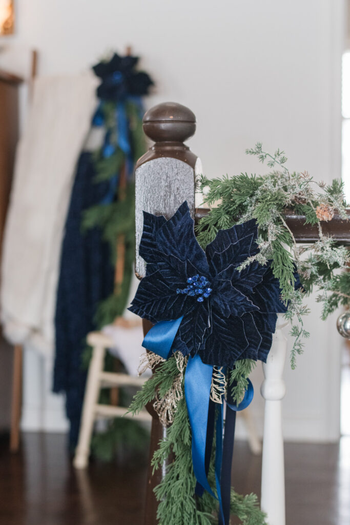 Blue poinsettia with blue satin and velvet ribbons hanging on a bannister with garland at Christmas