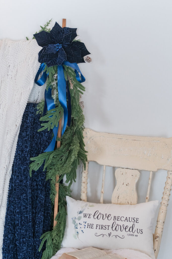 Garland hanging down a blanket ladder next to a chair with a pillow for Christmas