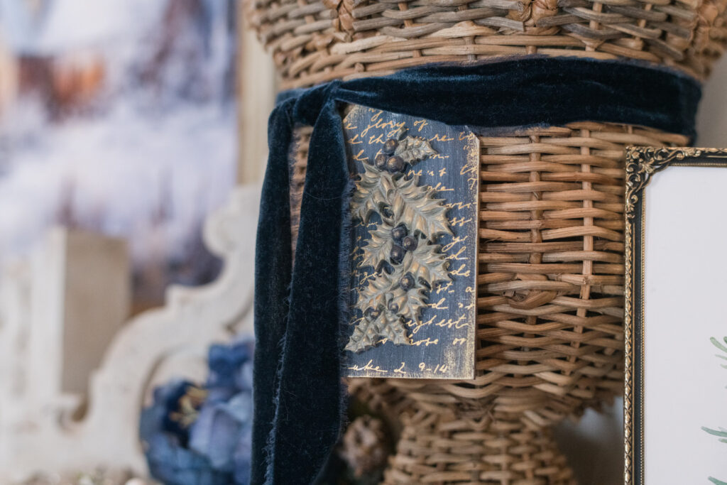 Handmade tag with Holly painted in blues Gold in soft greens hanging on a basket tied with blue velvet ribbon