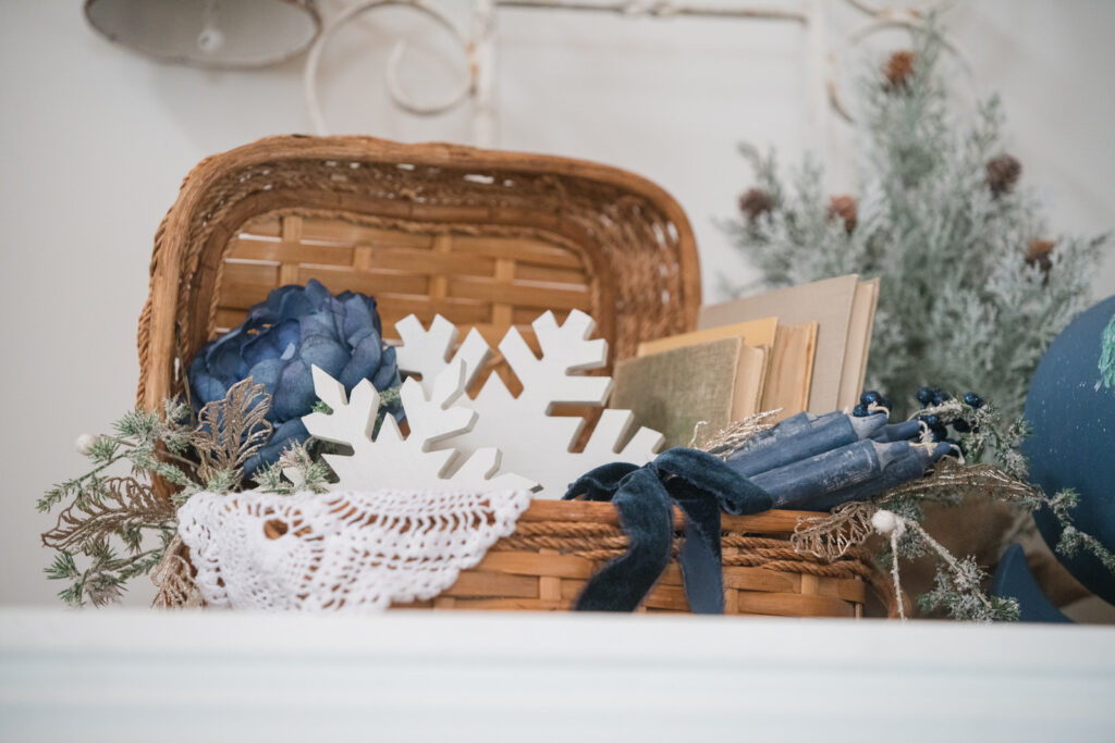Vintage basket filled with books, candles wrapped with a bow and snowflakes styled for Christmas