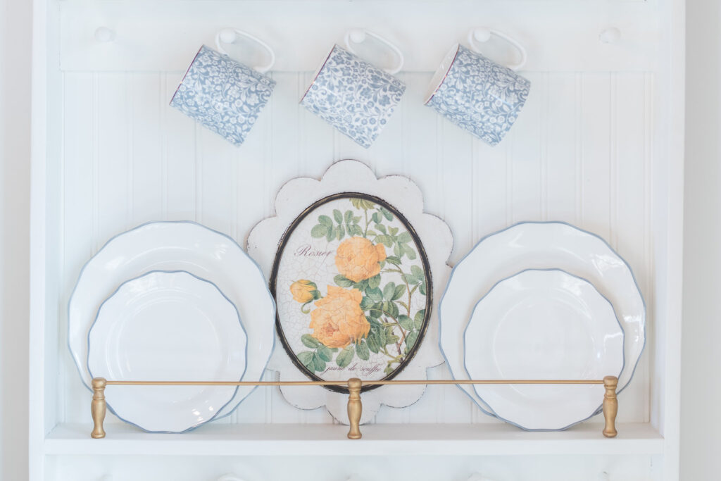 Scalloped oval frame on a plate rail with plate plates, and mugs hanging above
