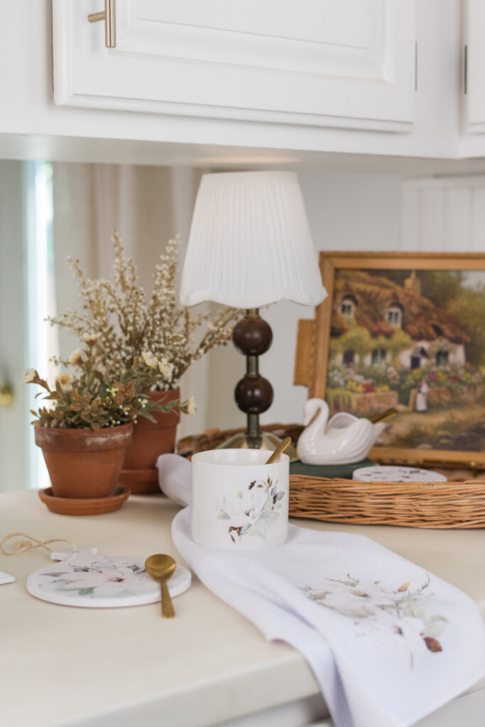 Magnolia collection coffee corner styled with a vintage lamp, wicker tray, a small swan dish holding gold spoons 
