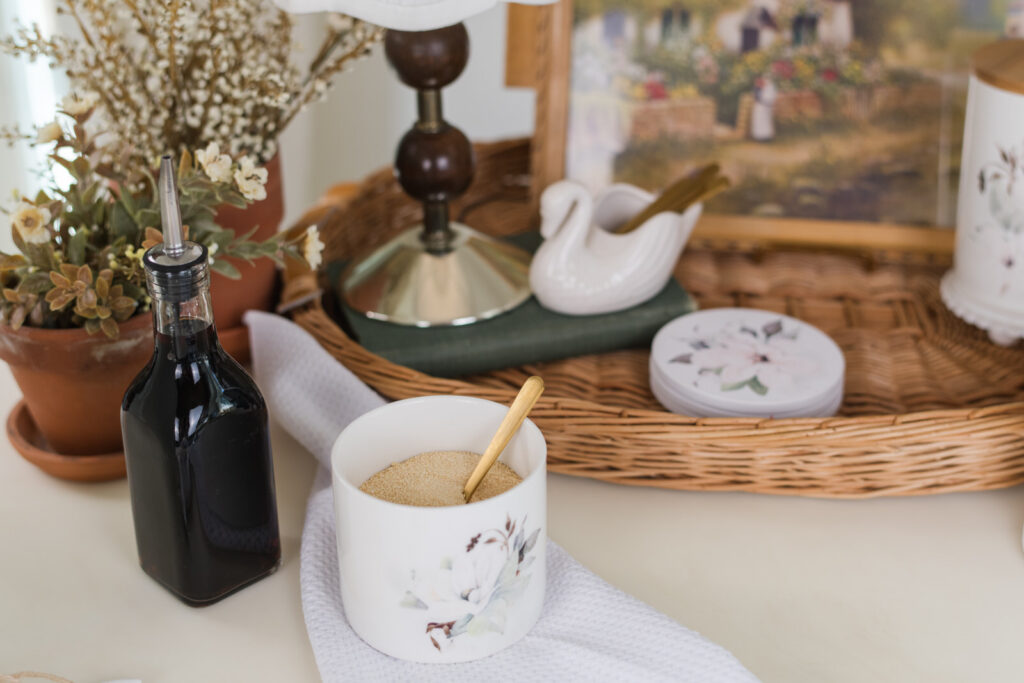 Small magnolia canister filled with sugar next to a vintage glass bottle, styled coffee bar 