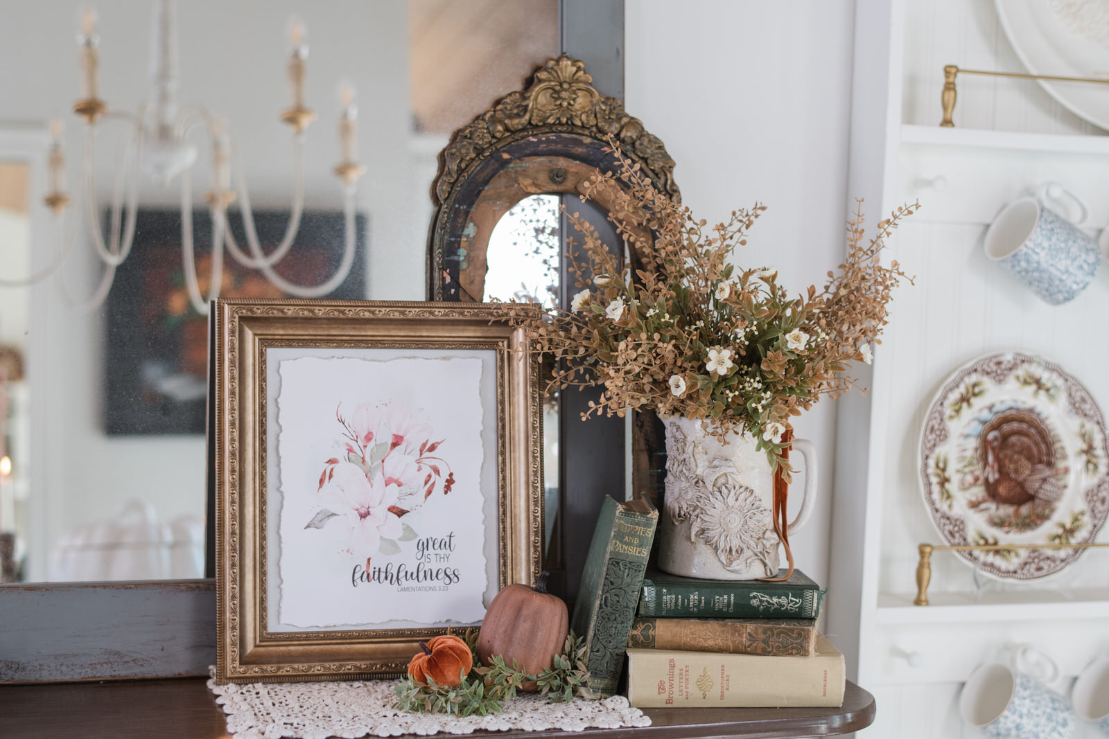 Old black frame with worn gold gilding behind a floral pitcher on a china cabinet