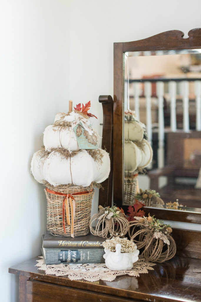 Close-up of a drop cloth pumpkin topiary with a leaf tag and raffia beside jute pumpkins on an entryway dresser