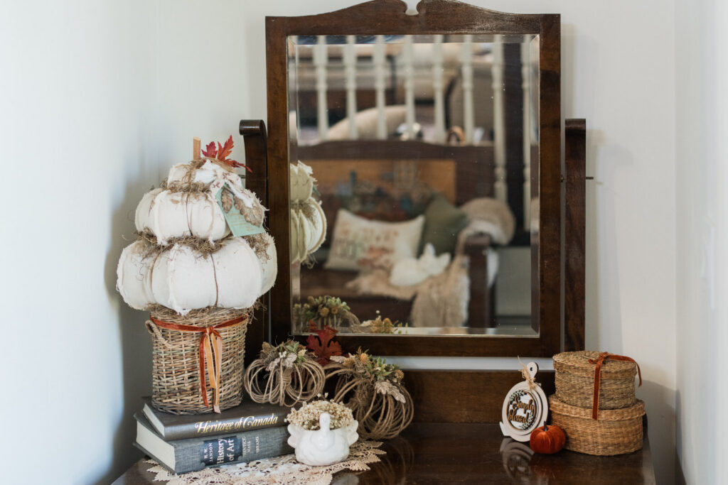Entryway dresser under a mirror styled for fall with a handmade pumpkin topiary, jute pumpkins, old books, baskets, and dried flowers