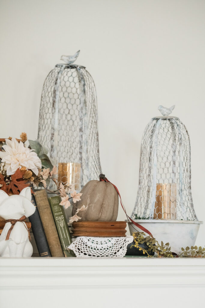 Close-up of white wire cloches, a small white fox, books, and pumpkins in a display above an entryway closet