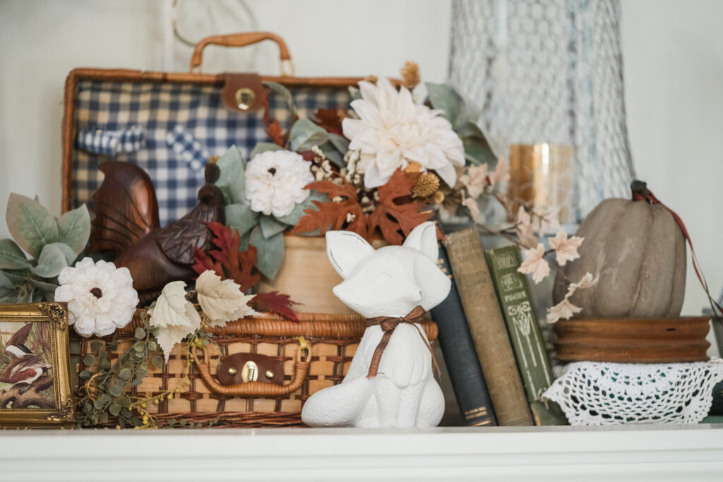 Close-up of an autumn scene in an entryway above a closet with fox vintage books, a wooden rooster, a vintage picnic basket, fall, stems, candlelight, and pumpkins