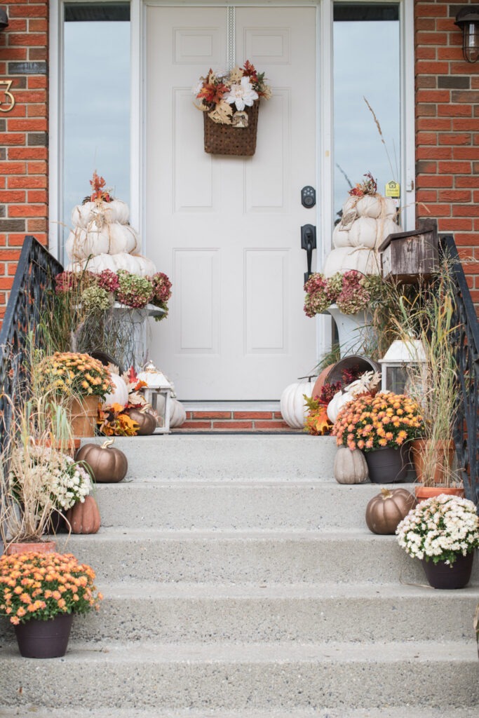 Orange and cream mums staggered along concrete steps beside an iron railing, with pumpkins and tall grasses